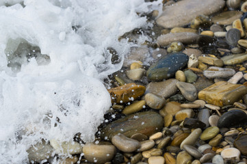 pebble stones on the sea beach, the rolling waves of the sea with foam