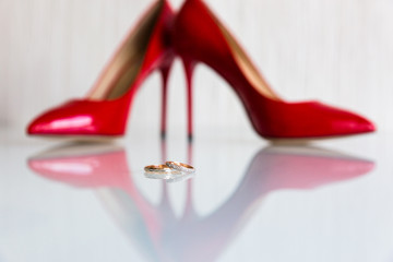 A pair of wedding rings on the mirror surface on the background of red heels
