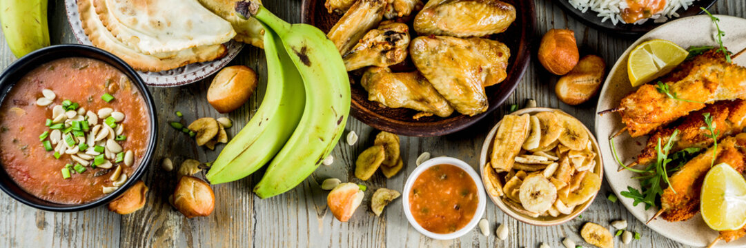 West african food concept. Traditional Wset African dishes assortment - peanut soup, jollof rice, grilled chicken wings, dry fried bananas plantains, nigerian chicken kebabs, meat pies, banner
