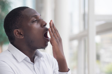 sleepy African man yawning; portrait of sleepy, tired, exhausted, sleepless African black man yawning; overwork or insomnia concept; young adult African man model