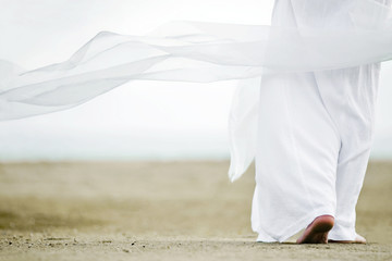 Photo of a man walking in a white robe on the sand. A picture from the back, a person is visible to...