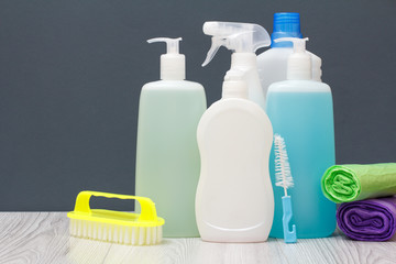 Bottles of dishwashing liquid, brushes and sponges on gray background.