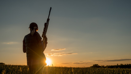 Sport shooting and hunting - woman with a rifle at sunset - obrazy, fototapety, plakaty