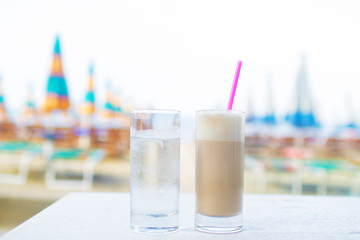 Glass of hot coffee and glass with water against sea background.