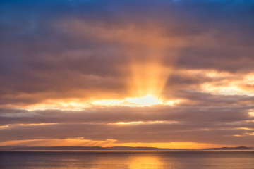 Golden Sun Rays Shining through Dark Clouds onto the Sea