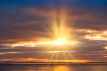 Fototapeta na wymiar Golden Sun Rays Shining through Dark Clouds onto the Sea