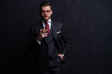 Handsome young business man enjoying a cigarette while standing on black background.