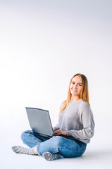 Naklejka premium The girl sits on a light background and works behind a laptop.