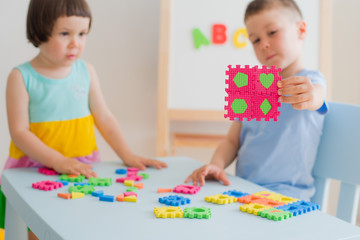 Fototapeta premium A boy and a girl collect a soft puzzle at the table. Brother and sister have fun playing together in the room.