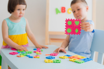 A boy and a girl collect a soft puzzle at the table. Brother and sister have fun playing together in the room.