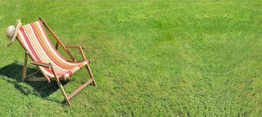 deckchair on greenery grass in a garden in panoramic size  - obrazy, fototapety, plakaty