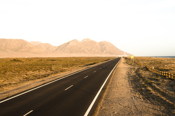 long straight road in the desert and a mountain at the end