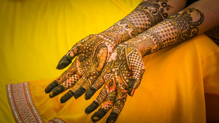 Henna painting, mehendi on bride's hands with the yellow dress background. Wedding preparation in...