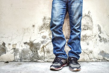 Obraz na płótnie Canvas Fashion jeans men wearing old shoes standing close to the background, old walls with cracks and black stains in the vintage background.