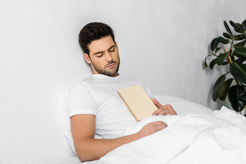 handsome young man sleeping in bed with book