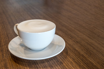 Close up a cup of coffee with milk froth on wooden table background