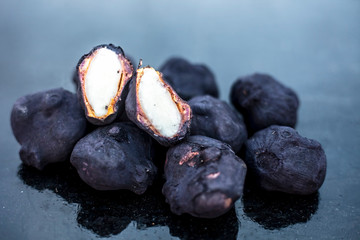 Close up of fresh organic raw water chestnuts on black colored wooden surface with one of them cut.