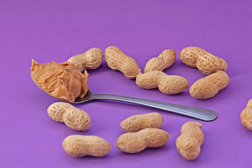 Spoon with peanut cream and peanuts on a purple background. Peanut butter. Spoon with nut butter
