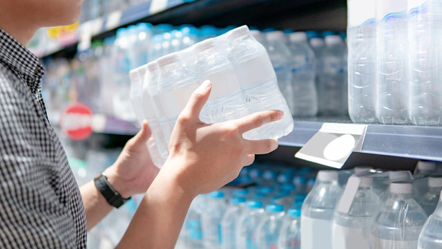 Male shopper picking pack of mineral water bottle from product shelf in supermarket. Customer shopping drinking water in grocery store. Healthy lifestyle
