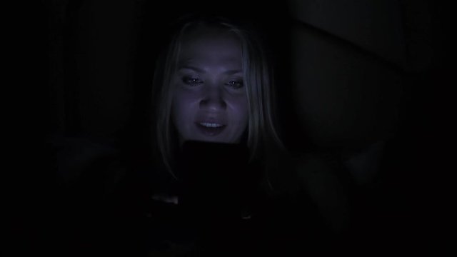 Woman with smartphone on bed at night.