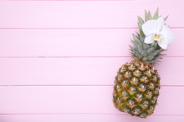 Ripe pineapple with orchid on a pink background with copy space