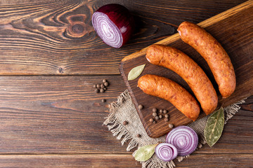 Smoked sausage with spices and onion on wooden background.