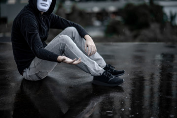 Reflection of mystery hoodie man in white mask sitting in the rain on rooftop of abandoned building. Bipolar disorder or Major depressive disorder. Depression concept