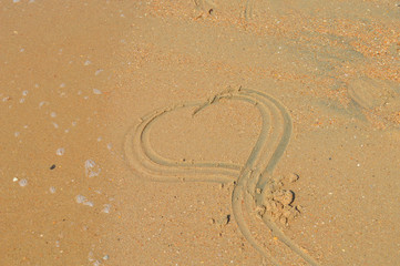 На морском песочном пляже нарисован символ сердца.