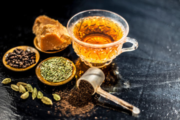 Close up of popular type of tea on wooden surface earlier dunked a lot i.e. Jaggery tea with ingredients like fennel,jaggery or gud,black pepper,tea leaves, milk, and green cardamom.