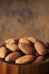 Almond nut in wooden bowl on wooden table with green leaf background