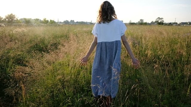 Woman walks across the field and hand touches high grass at sunset, slow motion