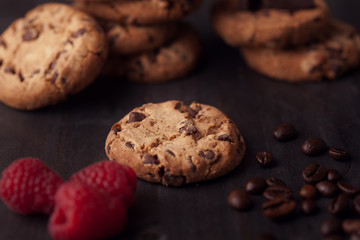 Chocolate chips cookies with red raspberries and coffee beans on dark old wooden table. Fresh out of the oven.