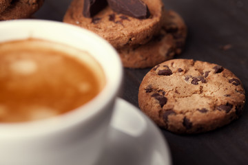 Homemade chocolate chip cookies and a cup of coffee on dark old wooden table. Sweet dessert.