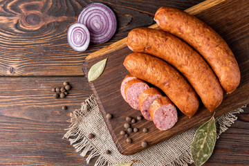 Smoked sausage with spices and onion on wooden background.