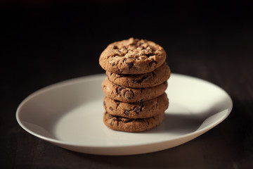 Pile of Delicious Chocolate Chip Cookies on a White Plate on old dark wooden table. Homemade cookies.