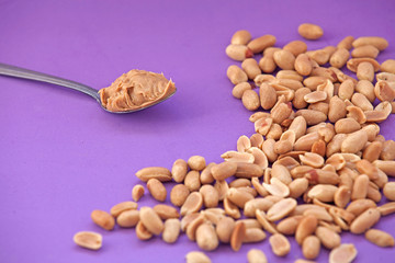 Spoon with peanut cream and peanuts on a purple background. Peanut butter. Spoon with nut butter
