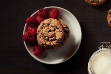 Top view of Chocolate chip cookies on white plate dark old wooden table with red raspberry. Healthy eating.
