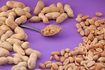 Spoon with peanut cream and peanuts on a purple background. Peanut butter. Spoon with nut butter