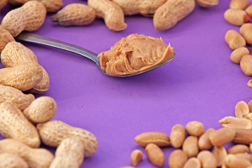 Spoon with peanut cream and peanuts on a purple background. Peanut butter. Spoon with nut butter