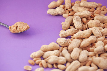 Spoon with peanut cream and peanuts on a purple background. Peanut butter. Spoon with nut butter