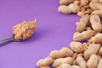 Spoon with peanut cream and peanuts on a purple background. Peanut butter. Spoon with nut butter