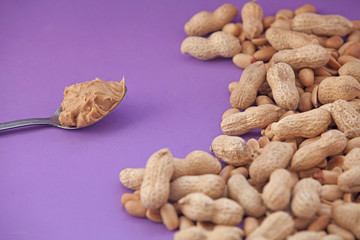 Spoon with peanut cream and peanuts on a purple background. Peanut butter. Spoon with nut butter