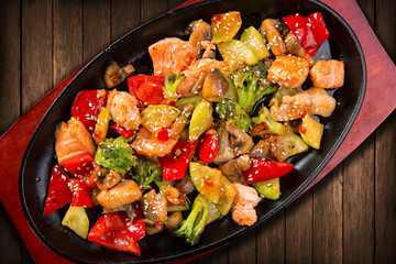 Fish salad with salmon pieces, vegetables, mushrooms and sesame, in a frying pan on the board