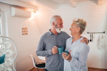 Obraz premium Portrait of a senior couple hugging while standing in bright room with mugs.