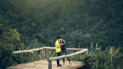 Fototapeta na wymiar traveler hike and camping in summer concept from asian couple take photo and see view with tropical forest background