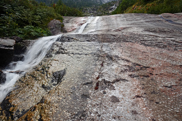 Panoramic view of a stream flowing on the steep rocky walls of Monte Rosa in Piedmont, Italy.