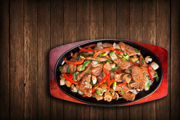 Slices of fried meat with onions, peppers, mushrooms, in a frying pan, on a board. View top.