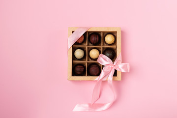 A set of different chocolates in a paper box with a satin pink color ribbon on a bright blue background.Flat layout.Copy space.
