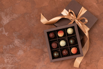 Fine chocolates in craft box with satin ribbon on a dark background. Place for design. Flat layout. Festive concept.