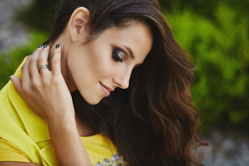 Fototapeta premium Beautiful and fashionable brunette model girl with professional bright makeup in stylish yellow sleeveless coat looks down and posing at city street